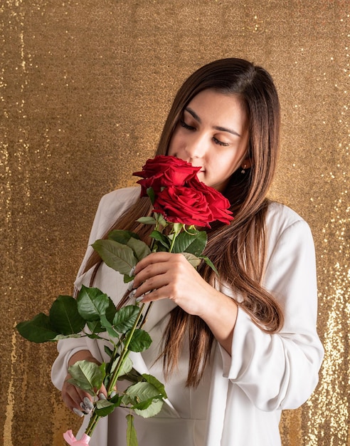 Jeune belle femme debout sur un fond brillant doré tenant des ballons rouges en forme de coeur