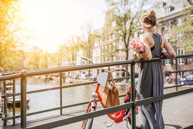 Jeune et belle femme debout avec vélo et fleurs sur le pont au-dessus du canal d'eau dans la ville d'Amsterdam