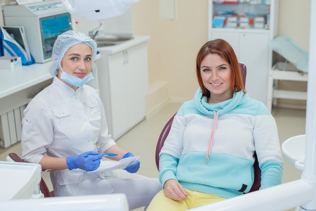 Jeune belle femme dentiste parle à son patient Femme rousse souriant à la réception chez le médecin Services dentaires