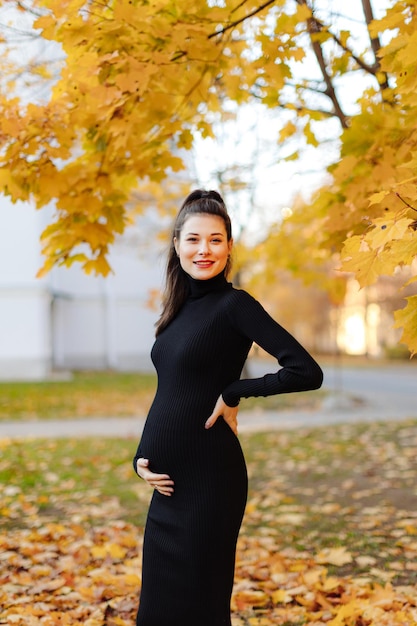 Jeune belle femme enceinte aux cheveux noirs dans une robe moulante noire posant sur un automne