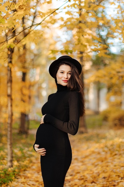 Jeune belle femme enceinte dans un chapeau aux cheveux noirs dans une robe moulante noire posant