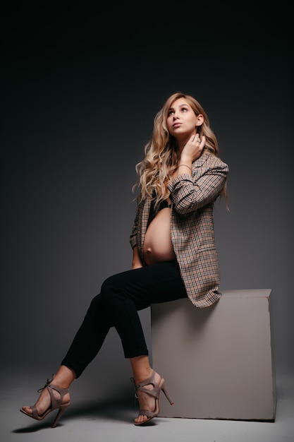 Jeune belle femme enceinte en veste sur mur noir