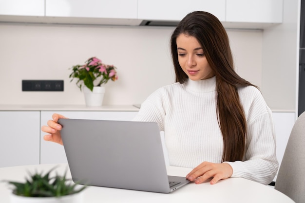 Une jeune belle femme est assise sur son lieu de travail et ouvre l'ordinateur portable pour travailler en ligne