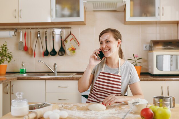 La jeune belle femme heureuse assise à une table avec de la farine et va préparer des gâteaux dans la cuisine. Cuisiner à la maison. Préparer la nourriture.