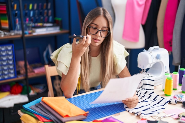 Jeune belle femme hispanique tailleur parlant sur un smartphone lisant un document à l'usine de vêtements