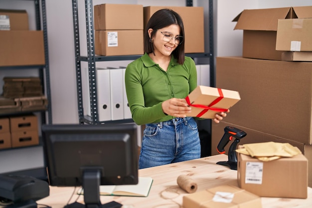 Jeune belle femme hispanique travailleur d'entreprise de commerce électronique souriant confiant tenant un cadeau au bureau