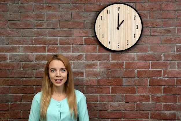 Jeune belle femme et horloge sur le mur de briques