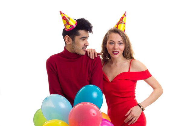 Jeune belle femme et jeune bel homme avec des chapeaux de fête tenant de nombreux ballons colorés