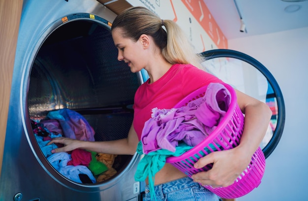 La jeune belle femme lave et sèche des vêtements dans la blanchisserie