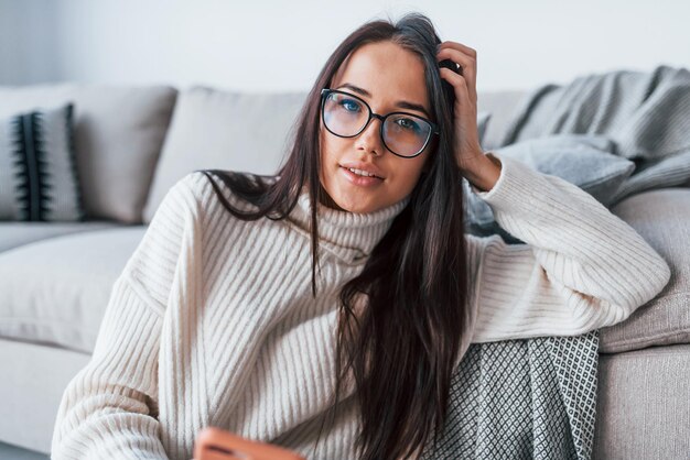 Jeune belle femme à lunettes assise seule à la maison avec un téléphone dans les mains.