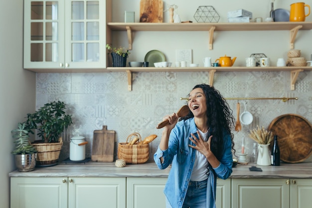 Jeune belle femme à la maison chantant et dansant dans la cuisine joyeuse femme latino-américaine