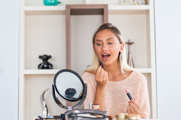 Jeune belle femme la maquillant près du miroir