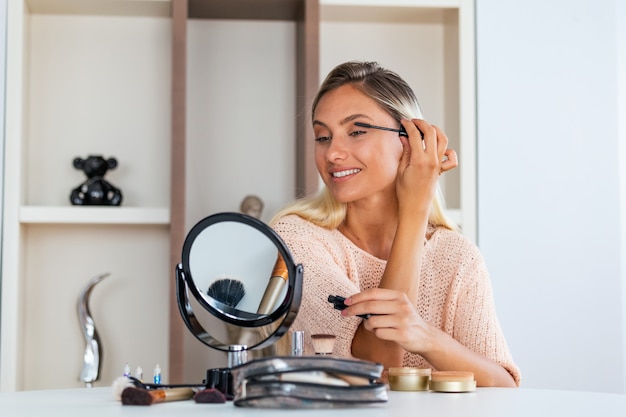 Jeune belle femme la maquillant près du miroir