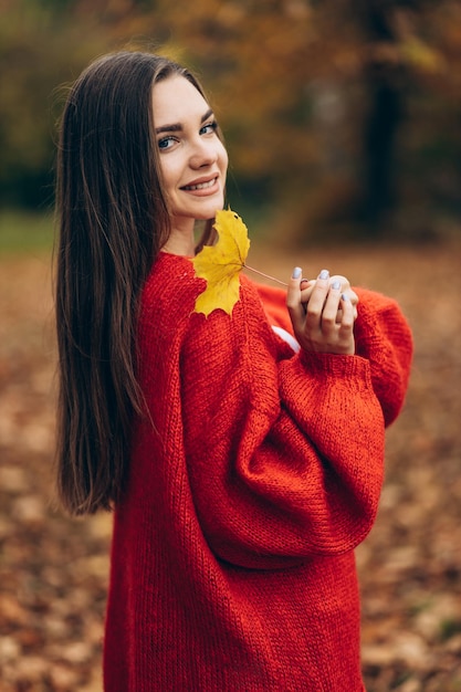 Jeune belle femme marchant dans le parc d'automne et tenant des feuilles