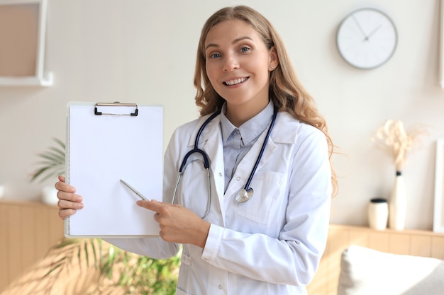 Jeune belle femme médecin en blouse blanche avec phonendoscope. Un médecin passe un appel vidéo en interaction via une conversation sur Internet avec un patient fournit de l'aide en ligne