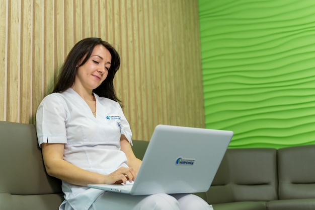 Jeune belle femme médecin lisant les résultats médicaux au bureau sur ordinateur portable. Arrière-plan de bureau d'hôpital moderne.