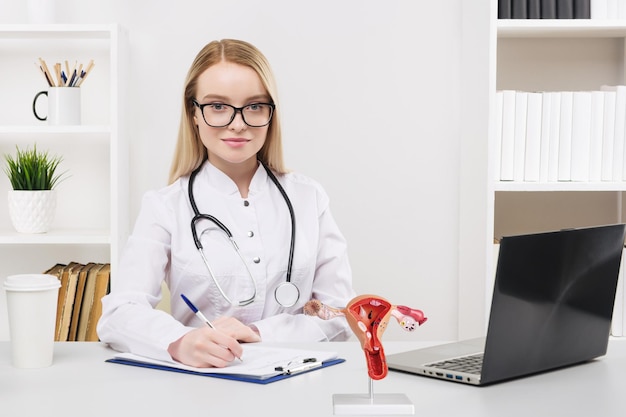 Jeune belle femme médecin travaillant heureux et sourire à l'hôpital assis sur la table Modèle de système reproducteur féminin sur le bureau