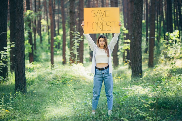 Jeune belle femme militante bénévole dans la forêt avec une affiche sauver la forêt