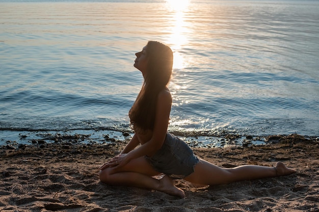 Jeune belle femme mince fait du yoga au bord de la mer sur le sable