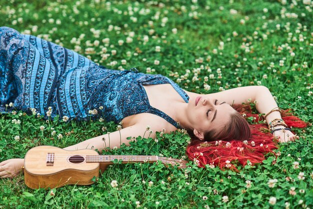 Jeune belle femme musicienne aux cheveux rouges au repos les yeux fermés allongée sur l'herbe un jour d'été.