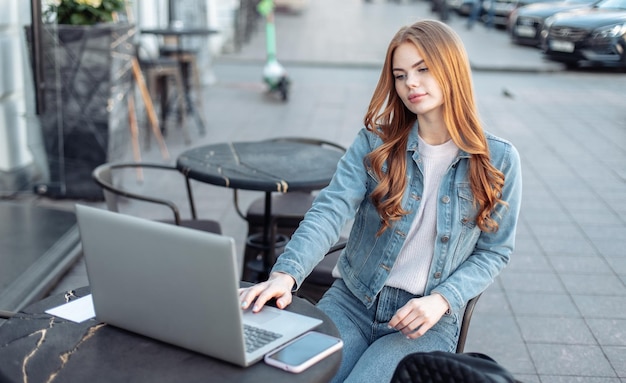 Jeune belle femme pigiste utilisant un ordinateur portable assis à table dans un café en plein air