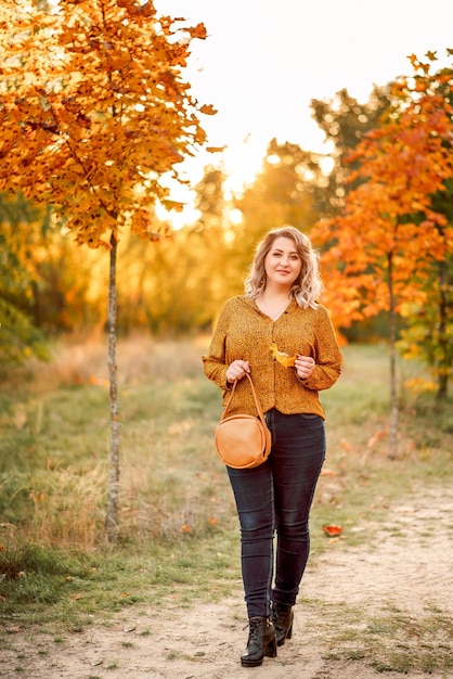 Jeune belle femme plussize dans une chemise orange et un jean se promène dans un parc en automne