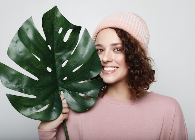 Jeune belle femme portant des vêtements décontractés roses tenant une feuille de monstera