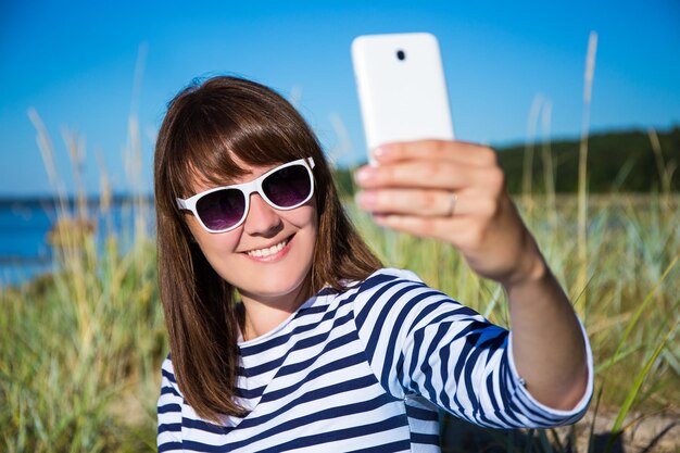 Jeune belle femme prenant une photo de selfie avec un téléphone intelligent sur la plage