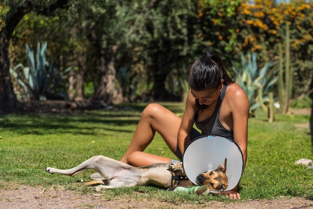 Jeune et belle femme prenant soin de son chien blessé sur l'herbe par une journée ensoleillée