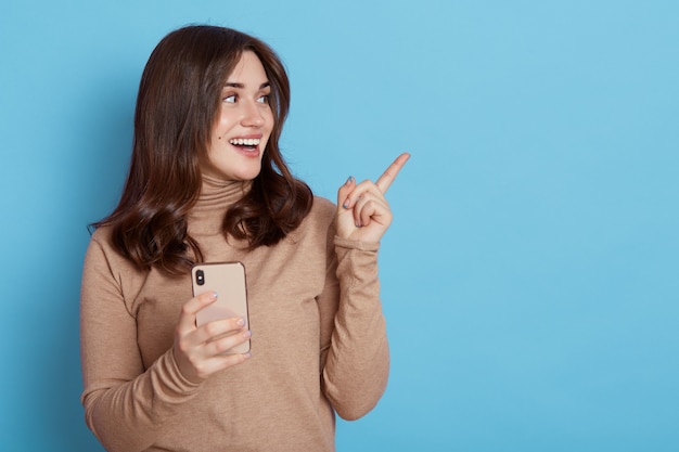 Jeune belle femme en pull beige, tenant en main un téléphone portable