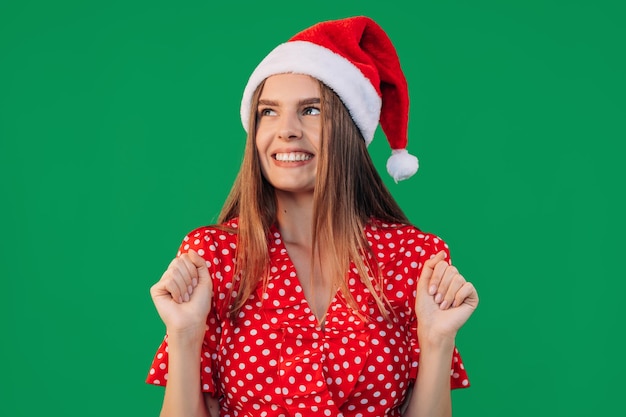 Jeune belle femme en robe et chapeau de père Noël est très heureuse et excitée fait un geste gagnant avec des sourires de mains levées et des cris de succès