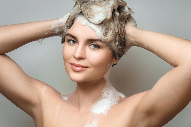 La jeune belle femme se lave les cheveux avec un shampooing