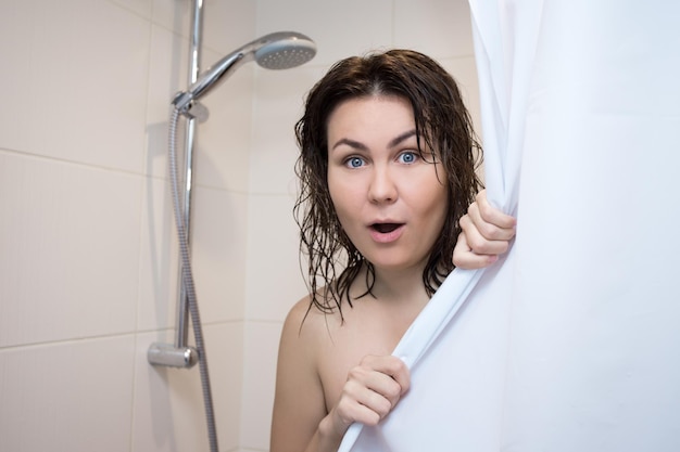 Jeune belle femme surprise couvrant son corps avec un rideau de douche