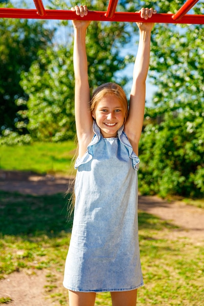 Jeune belle fille accrochée à la barre horizontale dans le parc