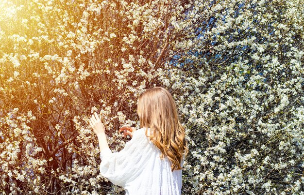 jeune belle fille à un arbre de fleurs en fleurs dans un parc rayons ensoleillés jolie femme