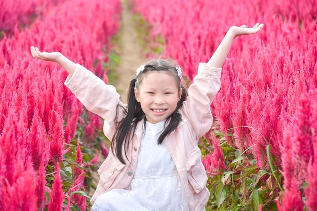 Jeune belle fille asiatique enfant souriant et levant les mains dans le champ de fleurs rouges.