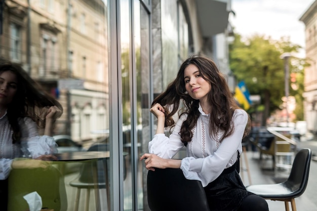 Jeune belle fille assise dans un café et attendant son heure d'été cappuccino