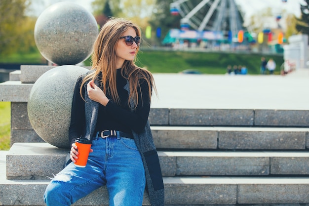 Jeune belle fille assise sur les marches avec du café dans des verres.