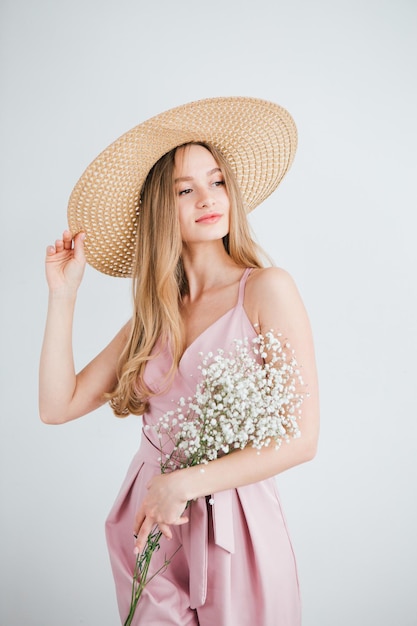 Jeune belle fille aux cheveux longs et chapeau posant avec un bouquet de fleurs blanches. Tonifiant.