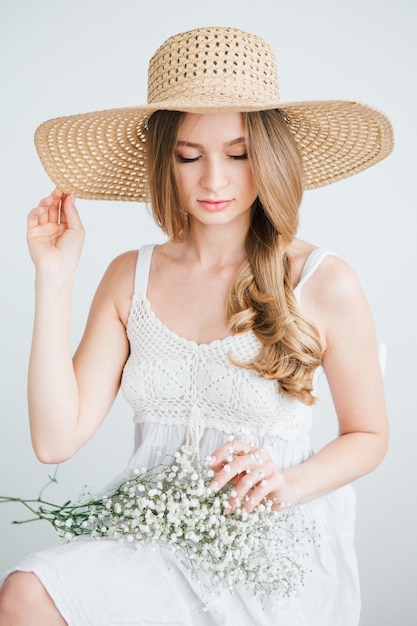 Jeune belle fille aux cheveux longs et chapeau posant avec un bouquet de fleurs blanches. Tonifiant.