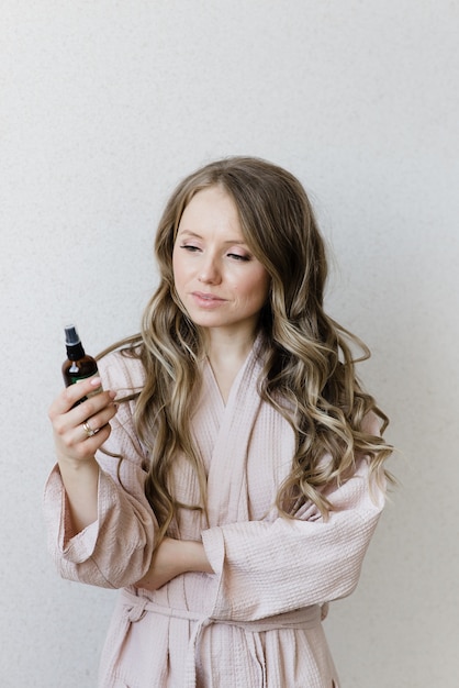 Jeune belle fille aux cheveux longs dans un peignoir examine le maquillage des cosmétiques