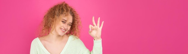 Jeune belle fille aux cheveux roux bouclés montre un signe ok à la caméra Un signe de succès et de bonne chance