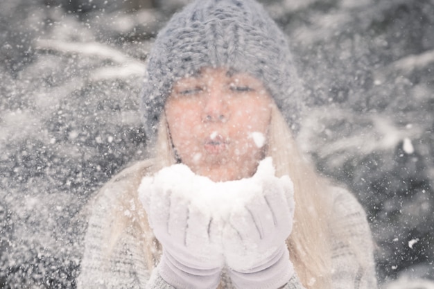 Jeune belle fille aux longs cheveux blancs joue des boules de neige. Elle s'amuse, jette de la neige et se réjouit des chutes de neige. Promenade d'hiver à l'extérieur.