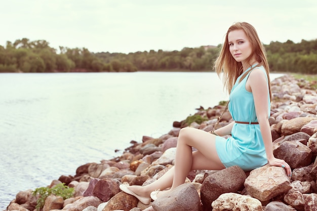 Jeune belle fille blonde assise sur les rochers, au bord de la rivière.