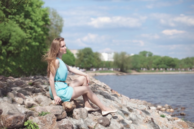 Jeune belle fille blonde assise sur les rochers, au bord de la rivière.