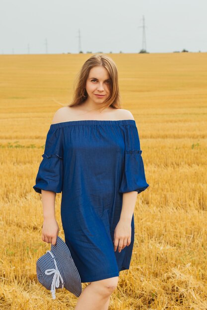 Jeune belle fille blonde au milieu d'un champ de blé .. Paysage d'été, beau temps. Robe en coton bleu, style éco. Beau chapeau rayé.