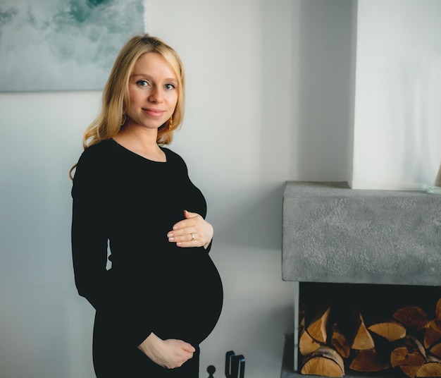 Jeune belle fille blonde caucasienne enceinte souriante heureuse debout dans le salon de la lumière blanche