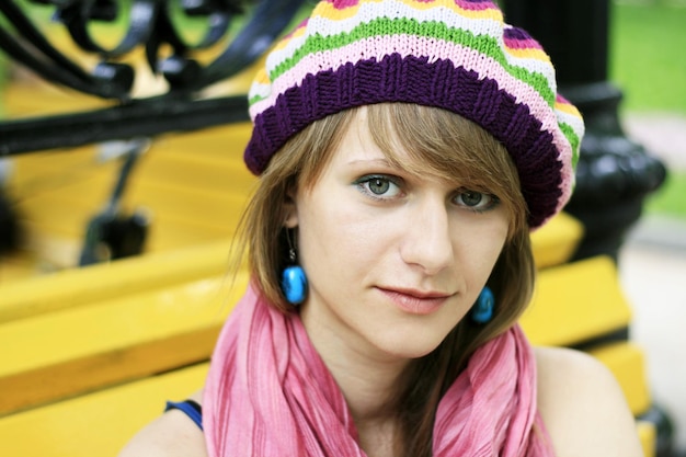 La jeune belle fille blonde dans un béret coloré s'assied sur un banc jaune en parc et regarde le c