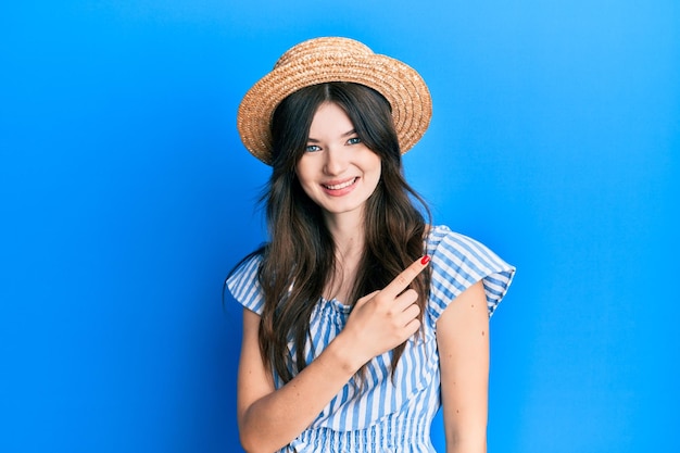 Jeune belle fille caucasienne portant un chapeau d'été souriant gai pointant avec la main et le doigt sur le côté