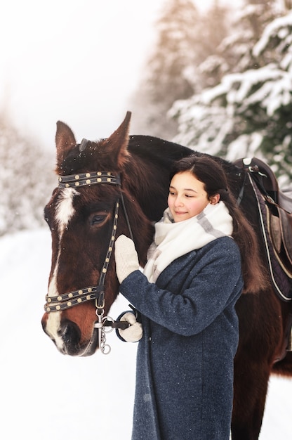 Jeune belle fille avec un cheval en hiver dans la nature. Amitié homme-animal